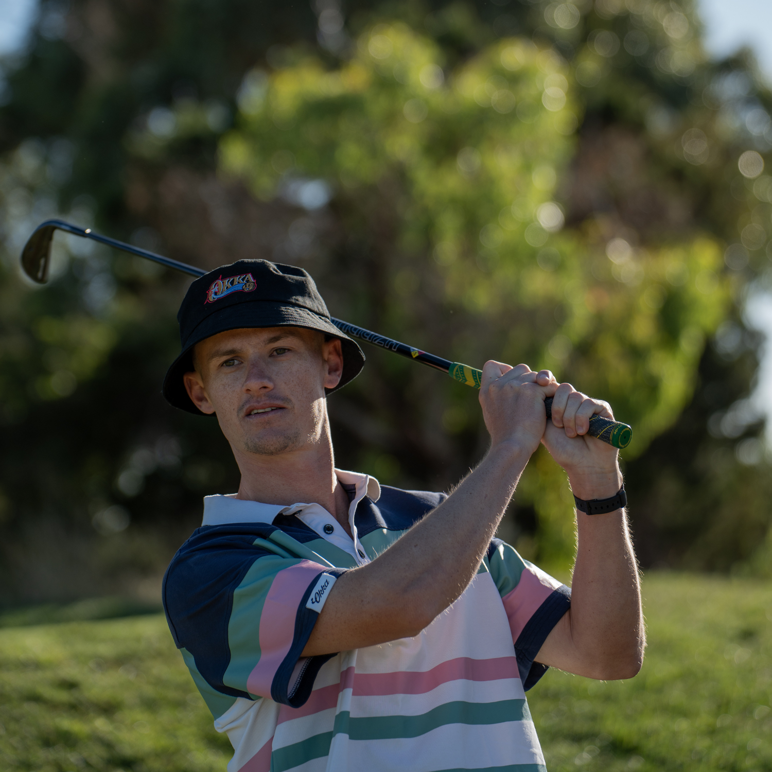Man swinging a golf club on a golf course with trees in the background